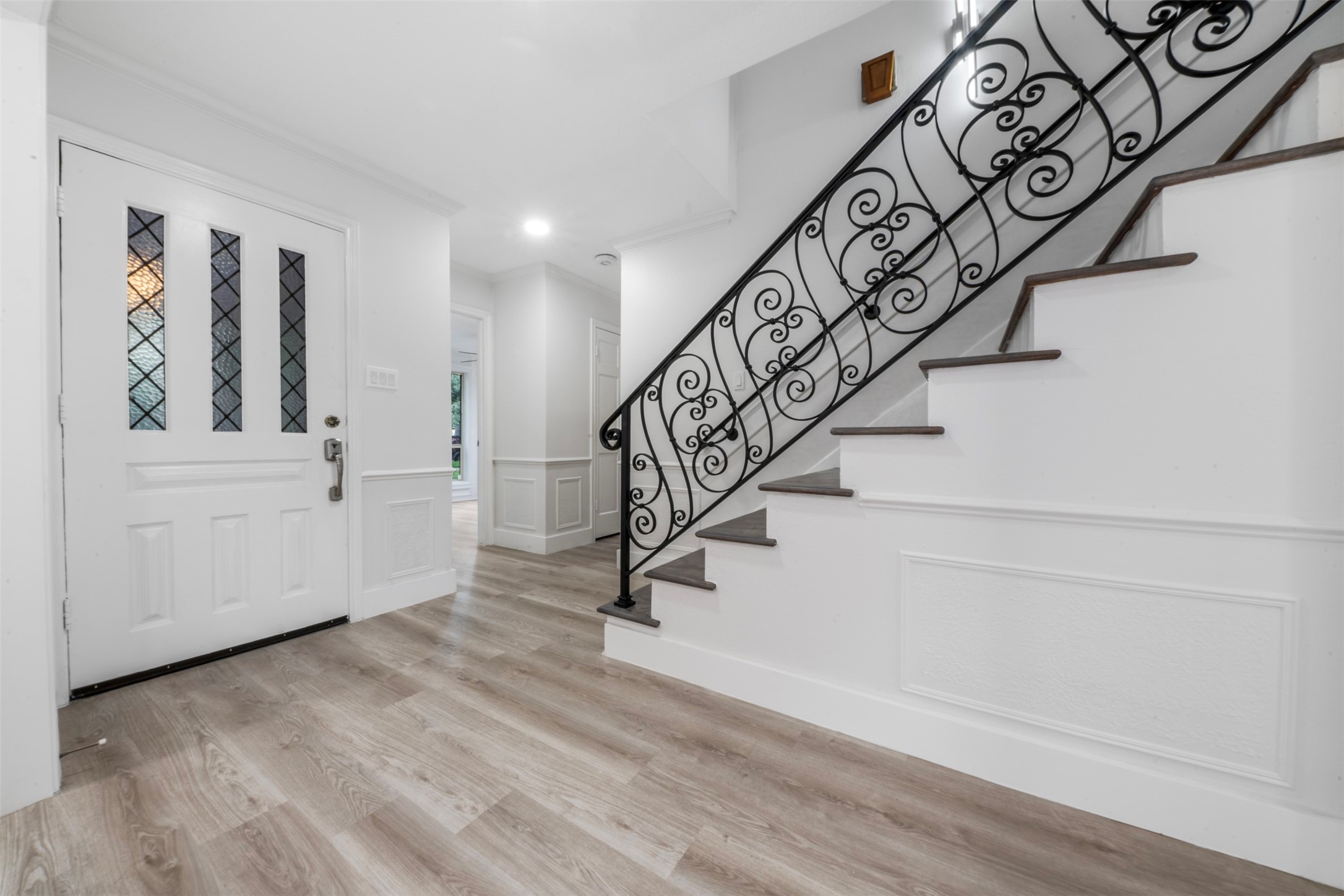 9543 Enstone Circle Spring, TX 77379 - Photo 2 of 50 This photo showcases a bright, welcoming foyer with a modern white door featuring decorative glass panels. The space includes elegant wood flooring and a staircase with an ornate wrought-iron railing, creating a stylish entrance.