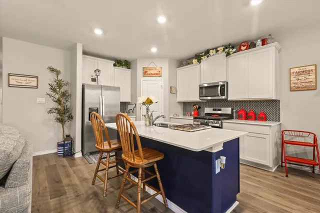 a kitchen with stainless steel appliances kitchen island granite countertop a sink dishwasher a stove a refrigerator a microwave oven with cabinets and wooden floor