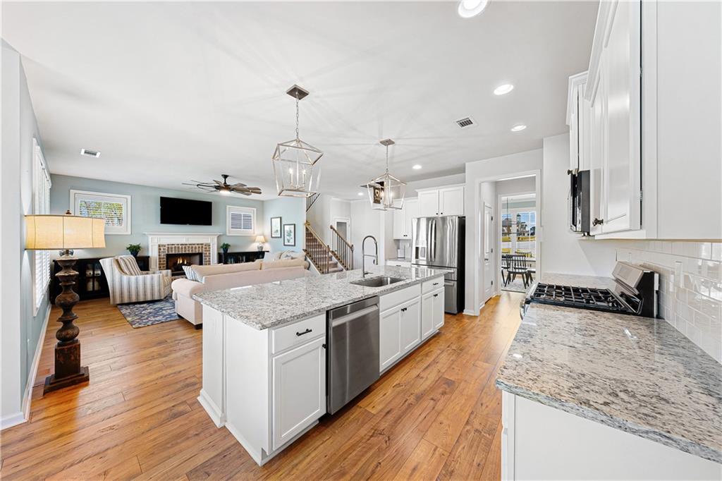 281 Greystone Court Winder, GA 30680 - Photo 17 of 71 a large kitchen with stainless steel appliances kitchen island granite countertop a large island a stove a sink dishwasher and a fireplace with wooden floor