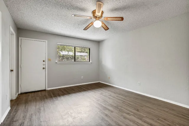 an empty room with wooden floor chandelier fan and windows