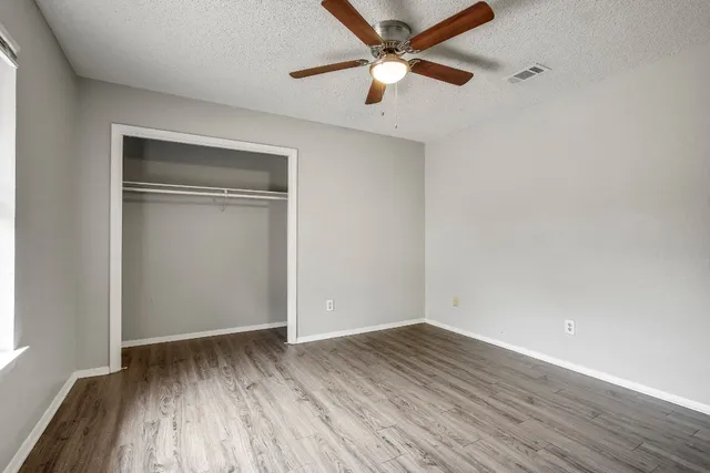 an empty room with wooden floor ceiling fan and windows