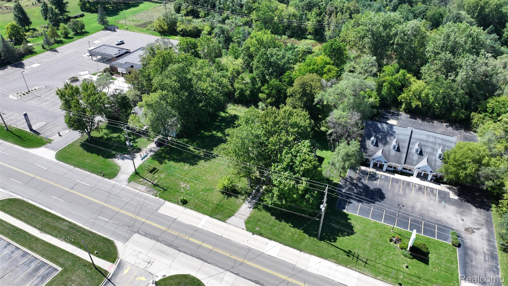 1220 Belsay Road Burton, MI 48509 - Photo 18 of 30 Commercial building featuring multiple dormer windows, a paved parking lot, and surrounding mature trees