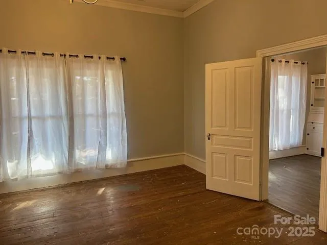 an empty room with wooden floor and windows with curtains