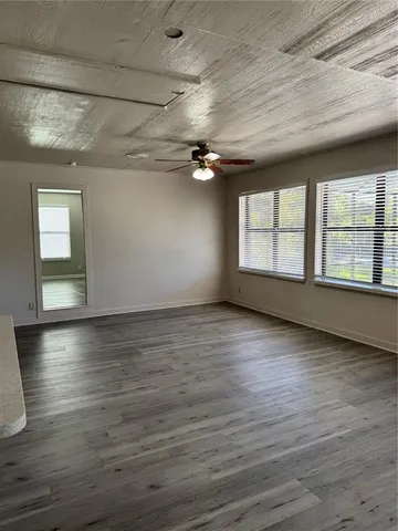 a view of an empty room with wooden floor and a kitchen