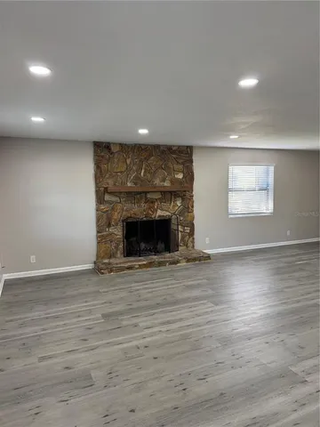 an empty room with wooden floor fireplace and windows