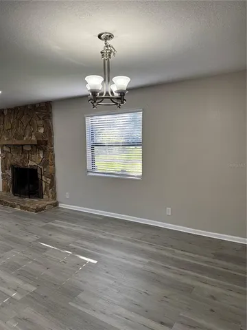 a view of an empty room with wooden floor fireplace and a window