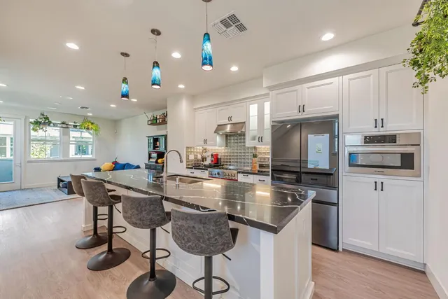 a kitchen with stainless steel appliances granite countertop a stove top oven a sink dishwasher a dining table and chairs with wooden floor