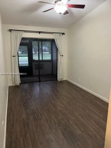 an empty room with wooden floor kitchen view and windows