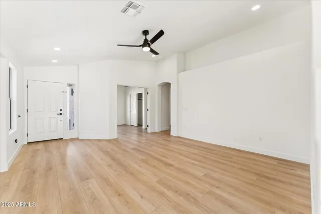 a view of an empty room with wooden floor and a ceiling fan