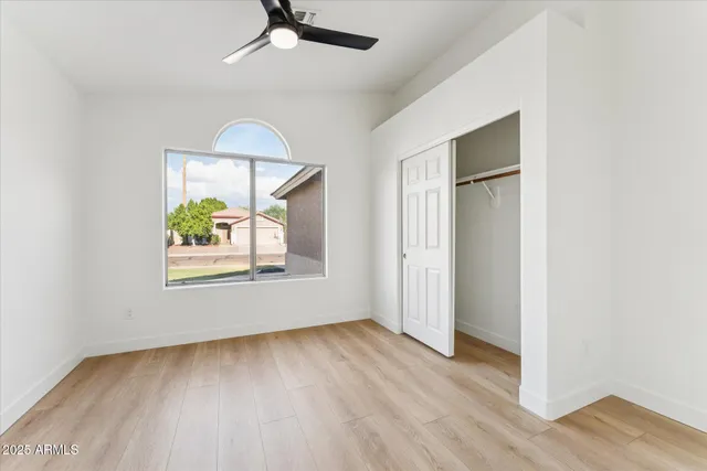 an empty room with wooden floor chandelier fan and windows
