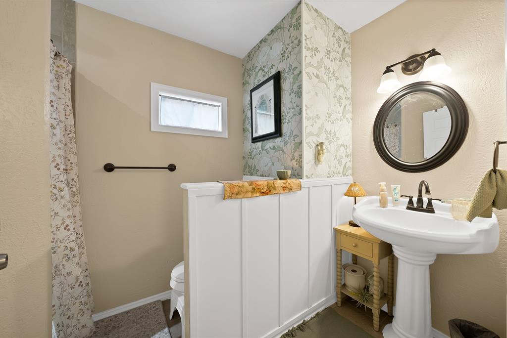 9519 County View Road Dallas, TX 75249 - Photo 15 of 31 Bathroom featuring a pedestal sink, a circular framed mirror, and a two-light vanity fixture