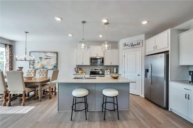 a kitchen with stainless steel appliances granite countertop a dining table chairs refrigerator and sink