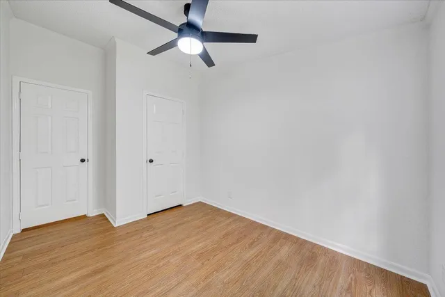 an empty room with wooden floor chandelier fan and windows