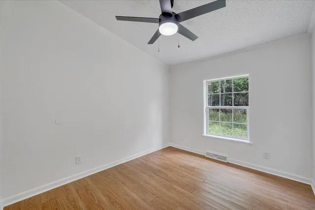 an empty room with wooden floor and a ceiling fan