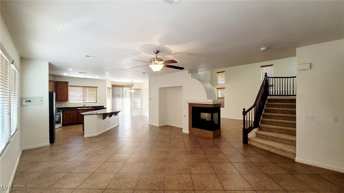5913 Altissimo Street North Las Vegas, NV 89081 - Photo 11 of 37 Unfurnished living room featuring a multi sided fireplace, a ceiling fan, light tile patterned flooring, stairway, and recessed lighting