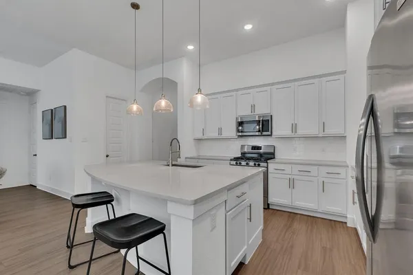 a kitchen with stainless steel appliances granite countertop a refrigerator a sink dishwasher a stove and white countertops with wooden floor