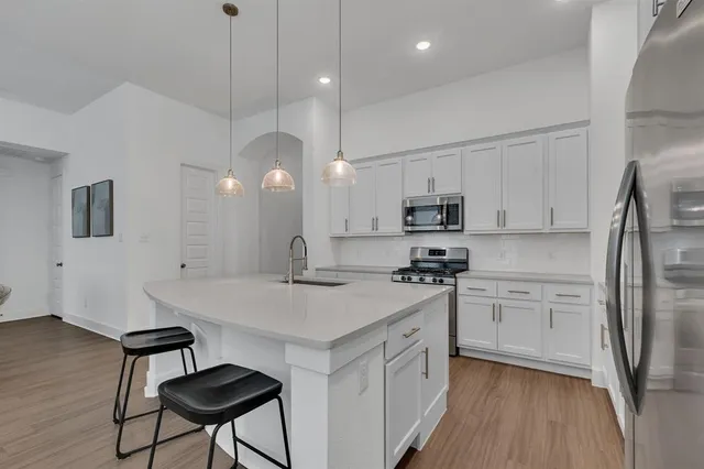 a kitchen with stainless steel appliances granite countertop a refrigerator a sink dishwasher a stove and white countertops with wooden floor