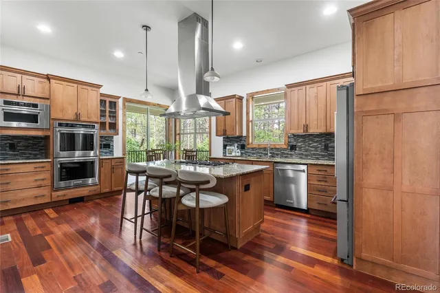 a kitchen with stainless steel appliances kitchen island granite countertop a stove a refrigerator a sink a dining table and chairs with wooden floor