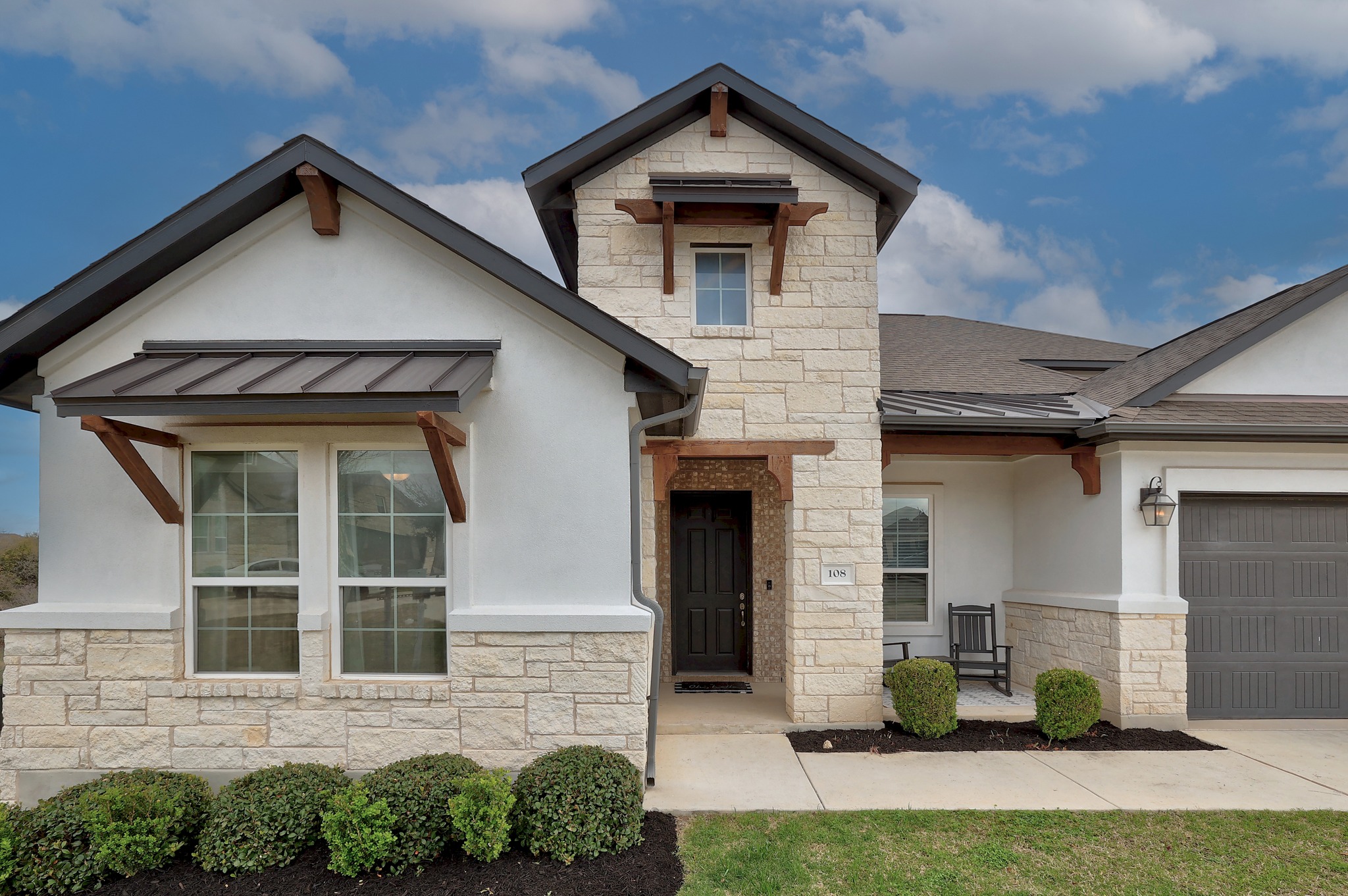 View of front facade featuring a standing seam roof, stone siding, and stucco siding