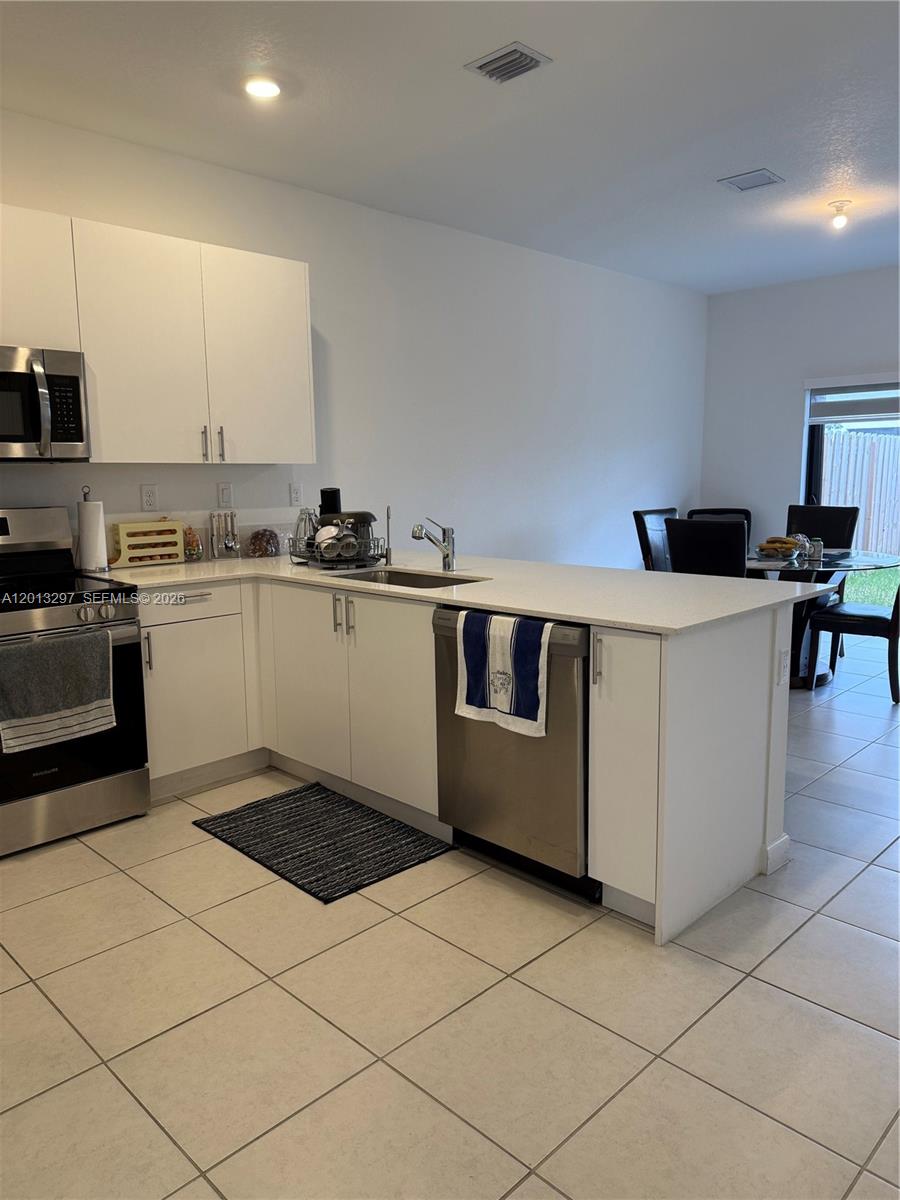 12955 Southwest 231st Terrace, Unit 12955 Miami, FL 33170 - Photo 2 of 26 a kitchen with stainless steel appliances a white stove top oven and white cabinets
