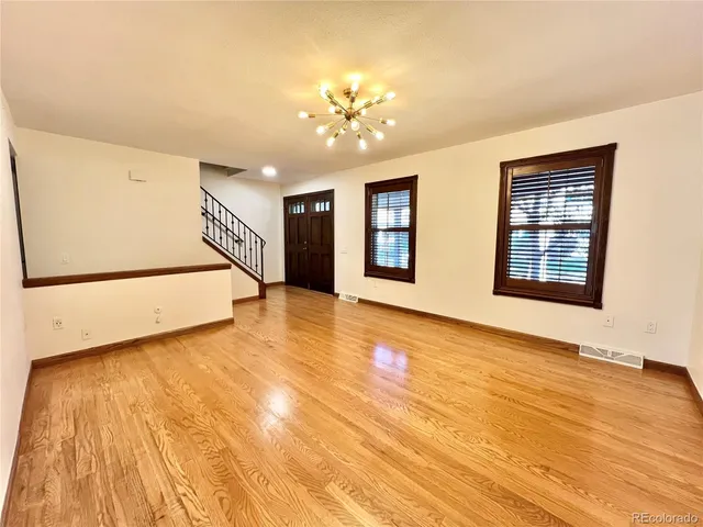 a view of an empty room with chandelier and wooden floor