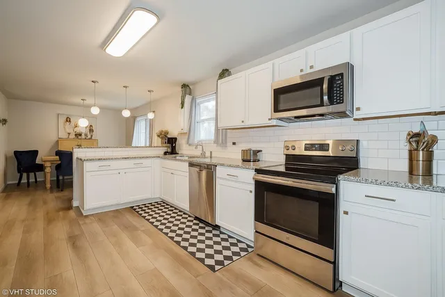a kitchen with stainless steel appliances white cabinets a sink a stove a microwave and wooden floors