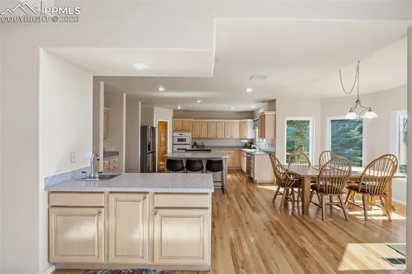 a kitchen with stainless steel appliances kitchen island granite countertop a stove a sink a dining table and chairs with wooden floor