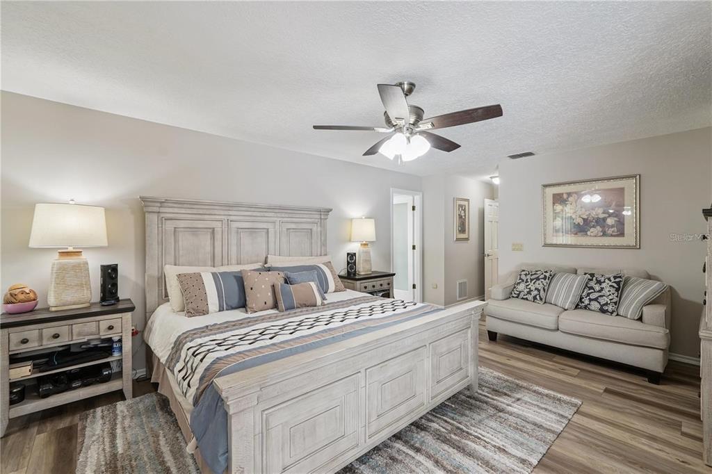 4603 Lake In The Woods Drive Spring Hill, FL 34607 - Photo 32 of 69 a spacious bedroom with a bed a couch and a chandelier