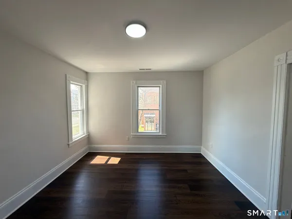 an empty room with wooden floor and windows with curtains