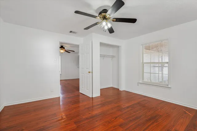 an empty room with wooden floor chandelier fan and windows