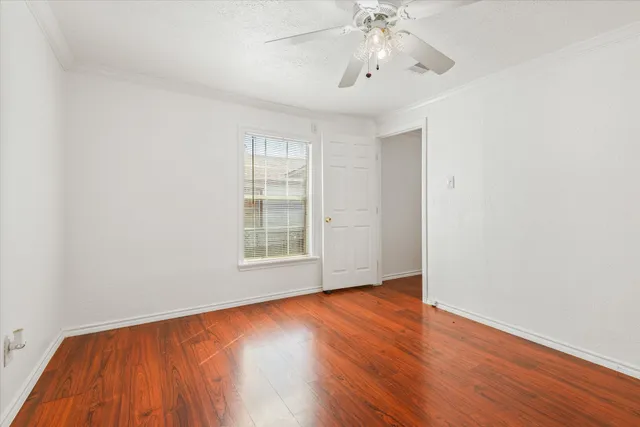 an empty room with wooden floor chandelier fan and windows