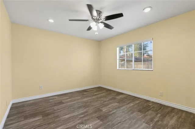 a view of an empty room with wooden floor and a ceiling fan