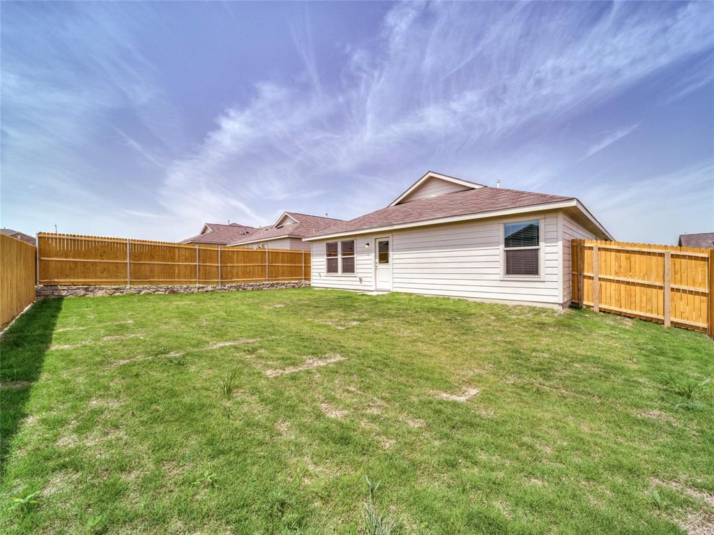 357 Sun Bluff Road Fort Worth, TX 76052 - Photo 24 of 35 Spacious backyard with a vibrant green lawn, featuring a wood fence with a stone base, siding exterior, and a rear entry door