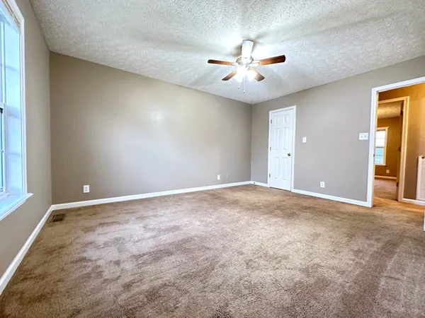 an empty room with chandelier fan and windows