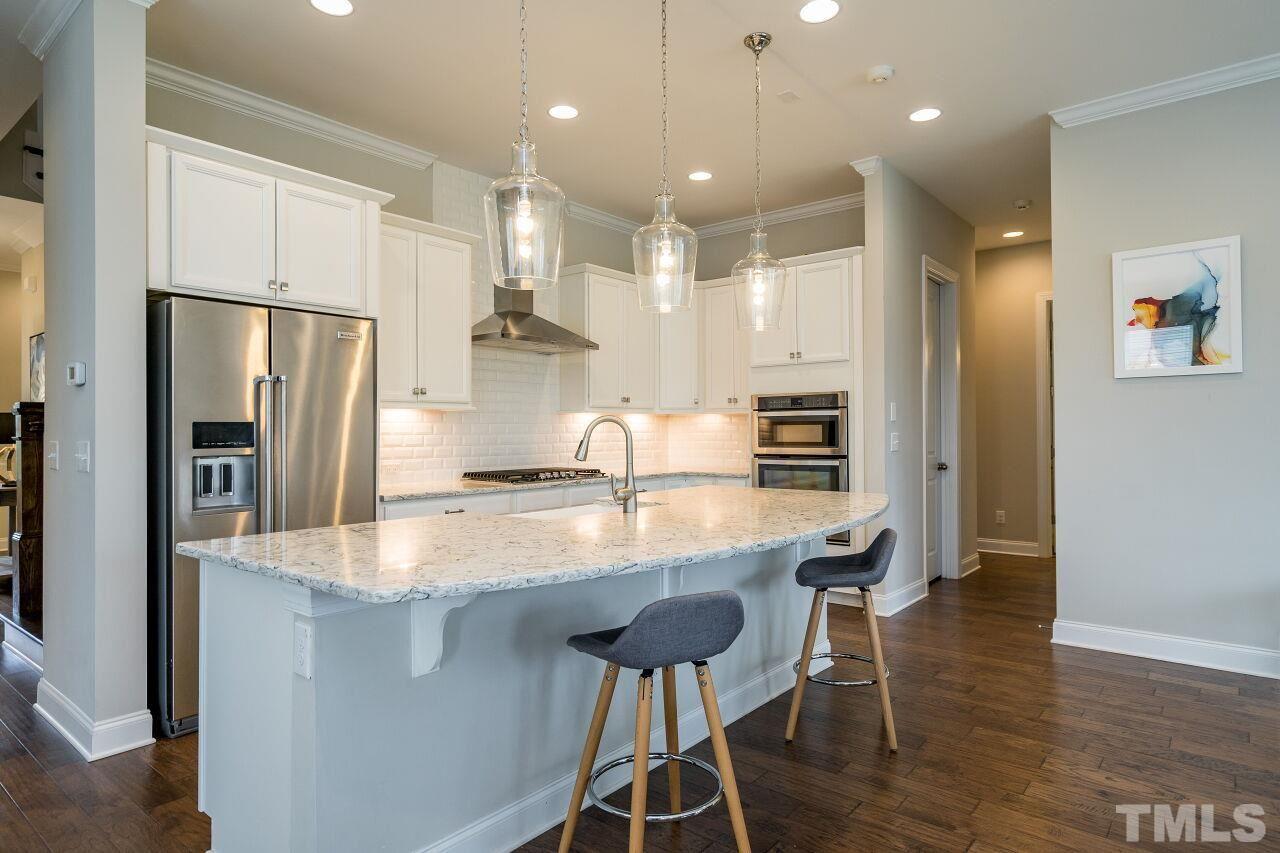 5264 Aleppo Lane Raleigh, NC 27613 - Photo 6 of 30 Sleek kitchen features white cabinets, subway tile, SS appliances, gas range, refrigerator, and large island.