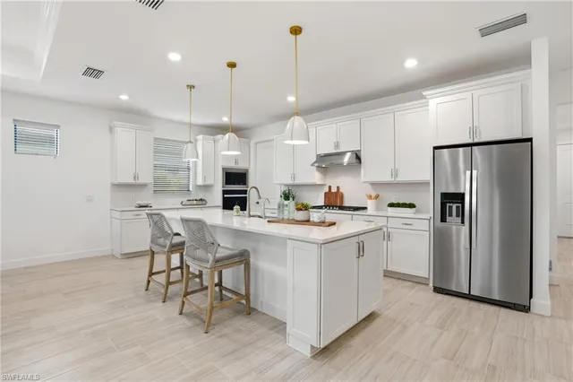 a kitchen with stainless steel appliances granite countertop a stove a sink a refrigerator and white cabinets with wooden floor