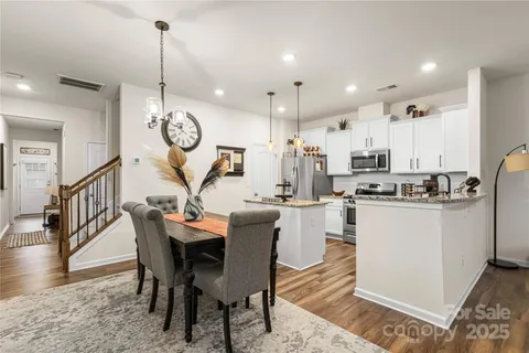a view of a dining room and livingroom with furniture wooden floor a rug a kitchen view and a chandelier