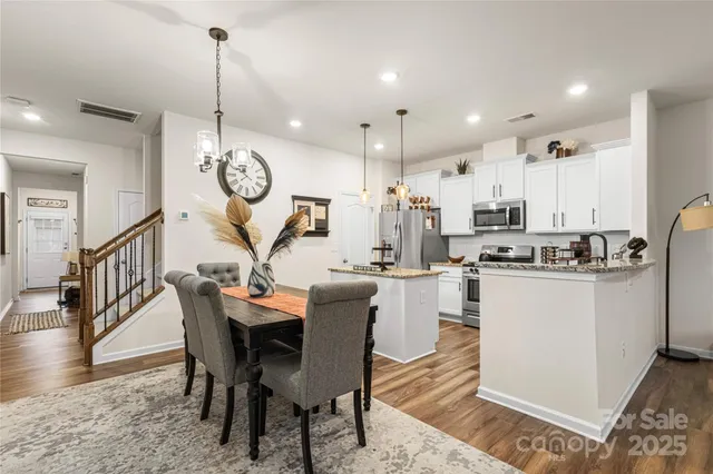 a view of a dining room and livingroom with furniture wooden floor a rug a kitchen view and a chandelier