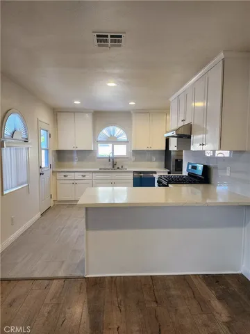 a large kitchen with stainless steel appliances a stove a sink a refrigerator white cabinets and wooden floor