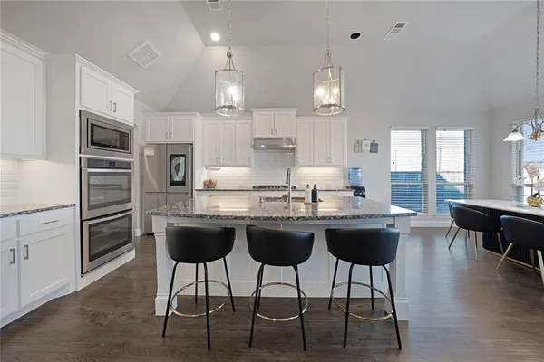 a kitchen with stainless steel appliances kitchen island granite countertop a table chairs sink and cabinets