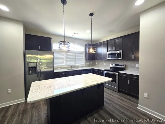 a kitchen with stainless steel appliances kitchen island granite countertop a sink a stove and a wooden floor