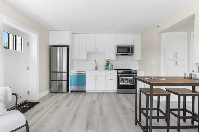 a kitchen with stainless steel appliances a stove a sink dishwasher a refrigerator with white cabinets and wooden floor