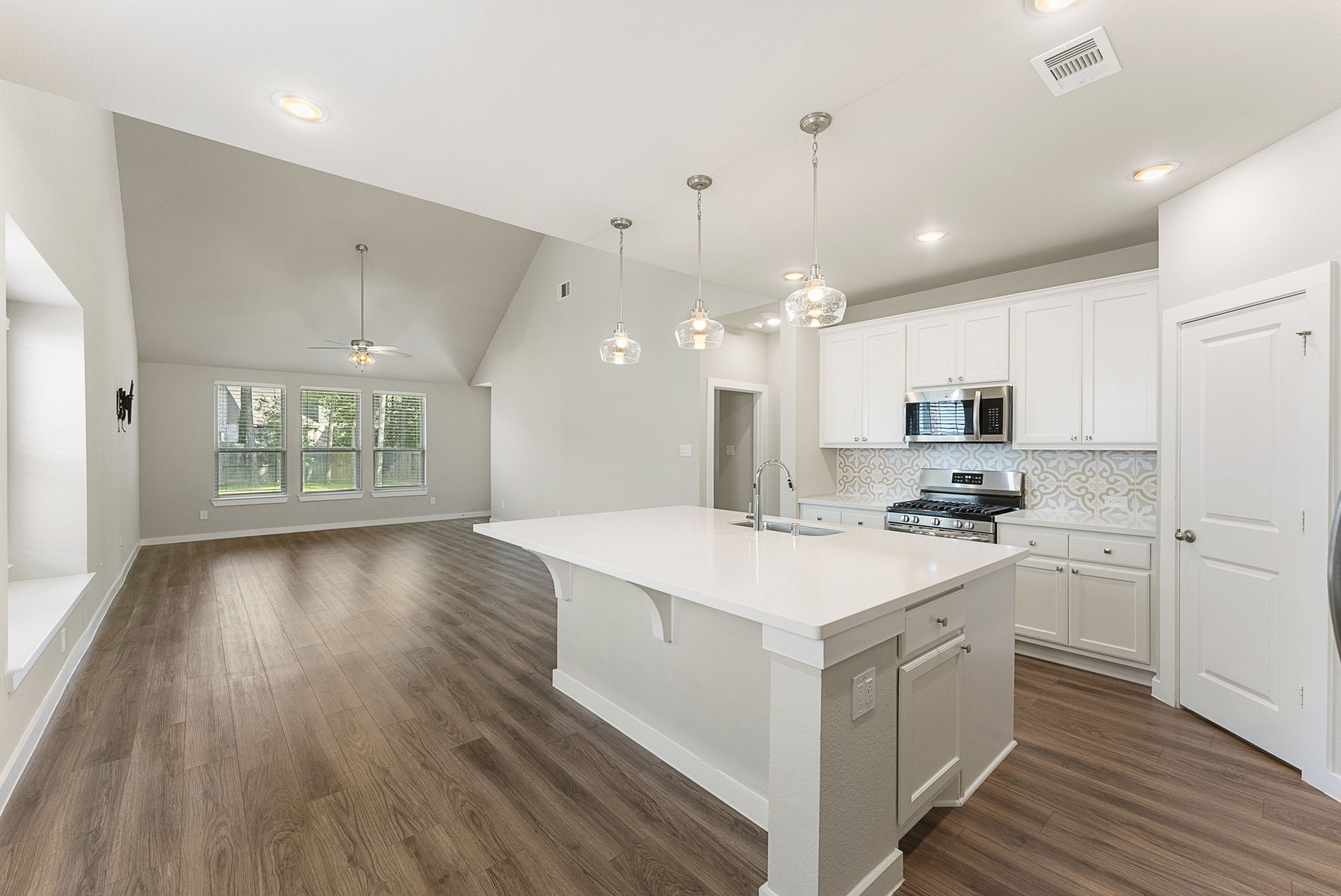 421 Soapberry Tree Court Conroe, TX 77318 - Photo 6 of 50 a large kitchen with kitchen island a sink dishwasher a stove a refrigerator and white cabinets with wooden floor