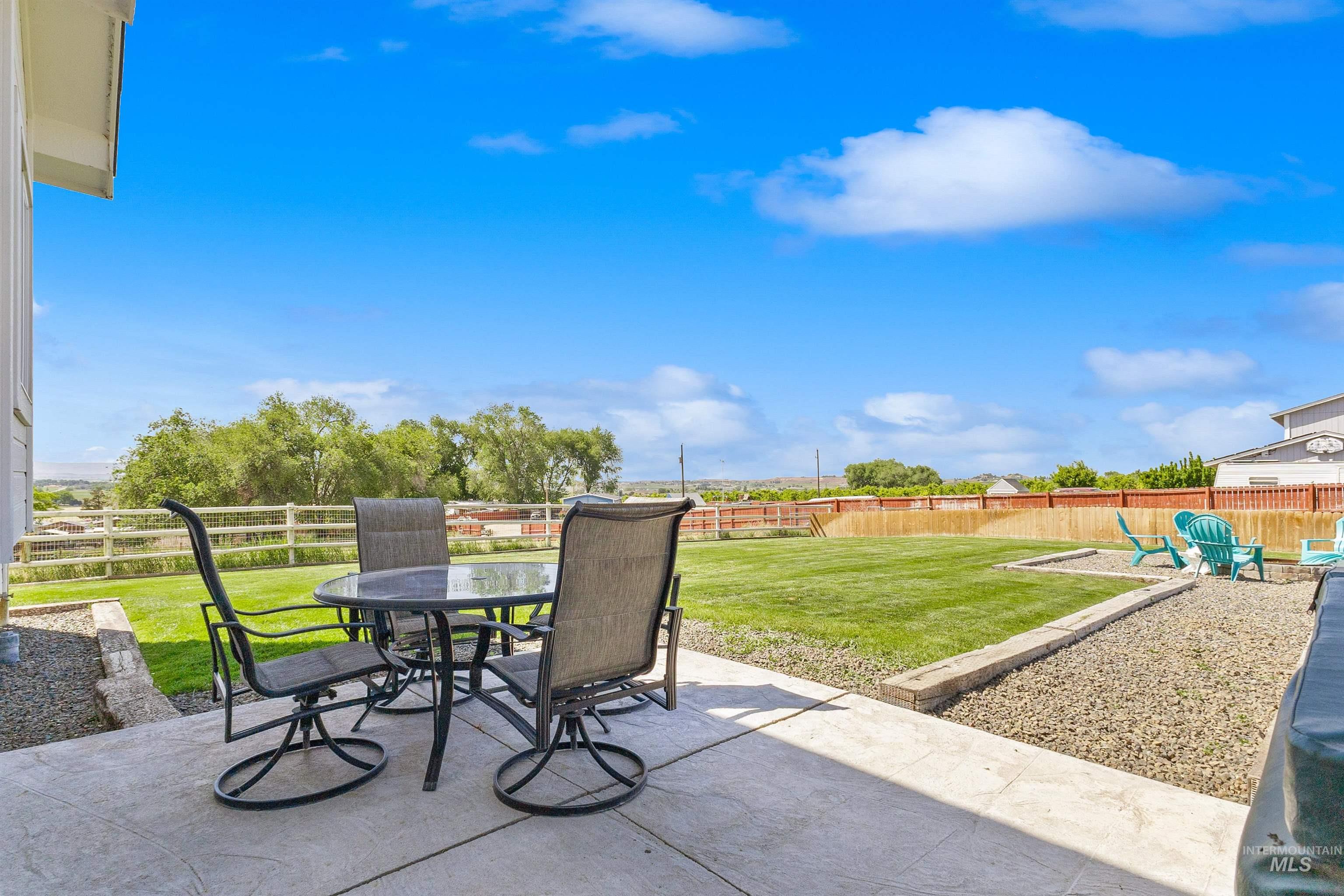 19876 Scotts Lane Caldwell, ID 83607 - Photo 12 of 44 Concrete patio featuring a large grassy area, gravel landscaping beds, and a wood fence enclosing the perimeter, eating space and the firepit