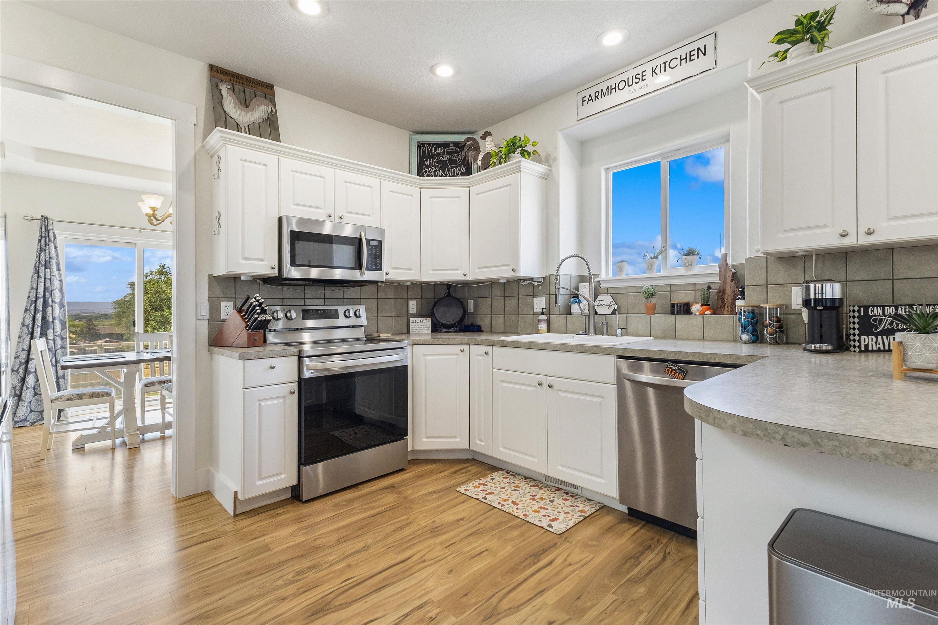 19876 Scotts Lane Caldwell, ID 83607 - Photo 24 of 44 Kitchen featuring white cabinetry, wood-finish flooring, stainless steel appliances, and a tiled backsplash