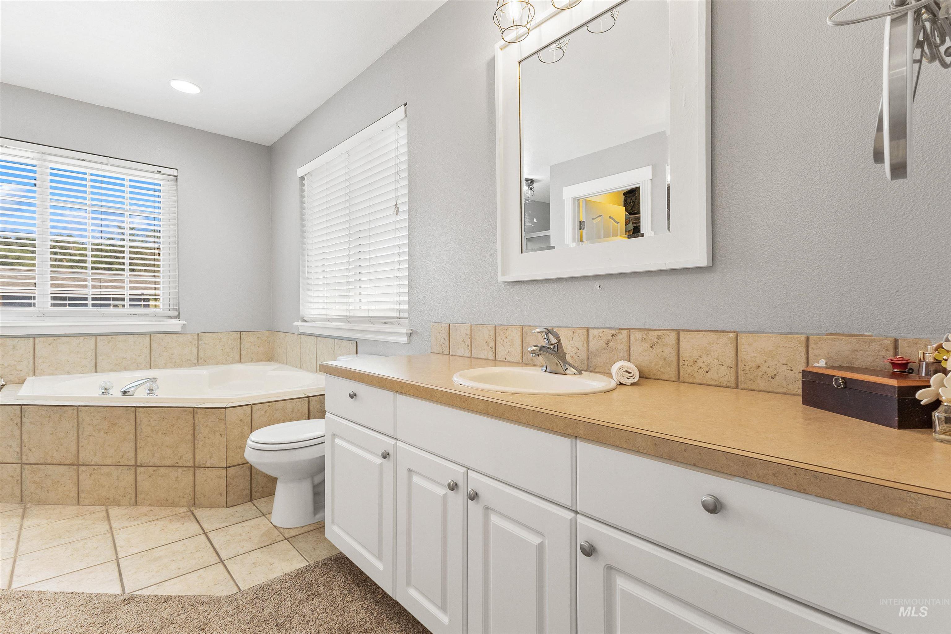 19876 Scotts Lane Caldwell, ID 83607 - Photo 37 of 44 Bathroom featuring an integrated corner bathtub with tile surround, a single vanity with an oval sink, white cabinetry, a tiled backsplash, and a framed vanity mirror