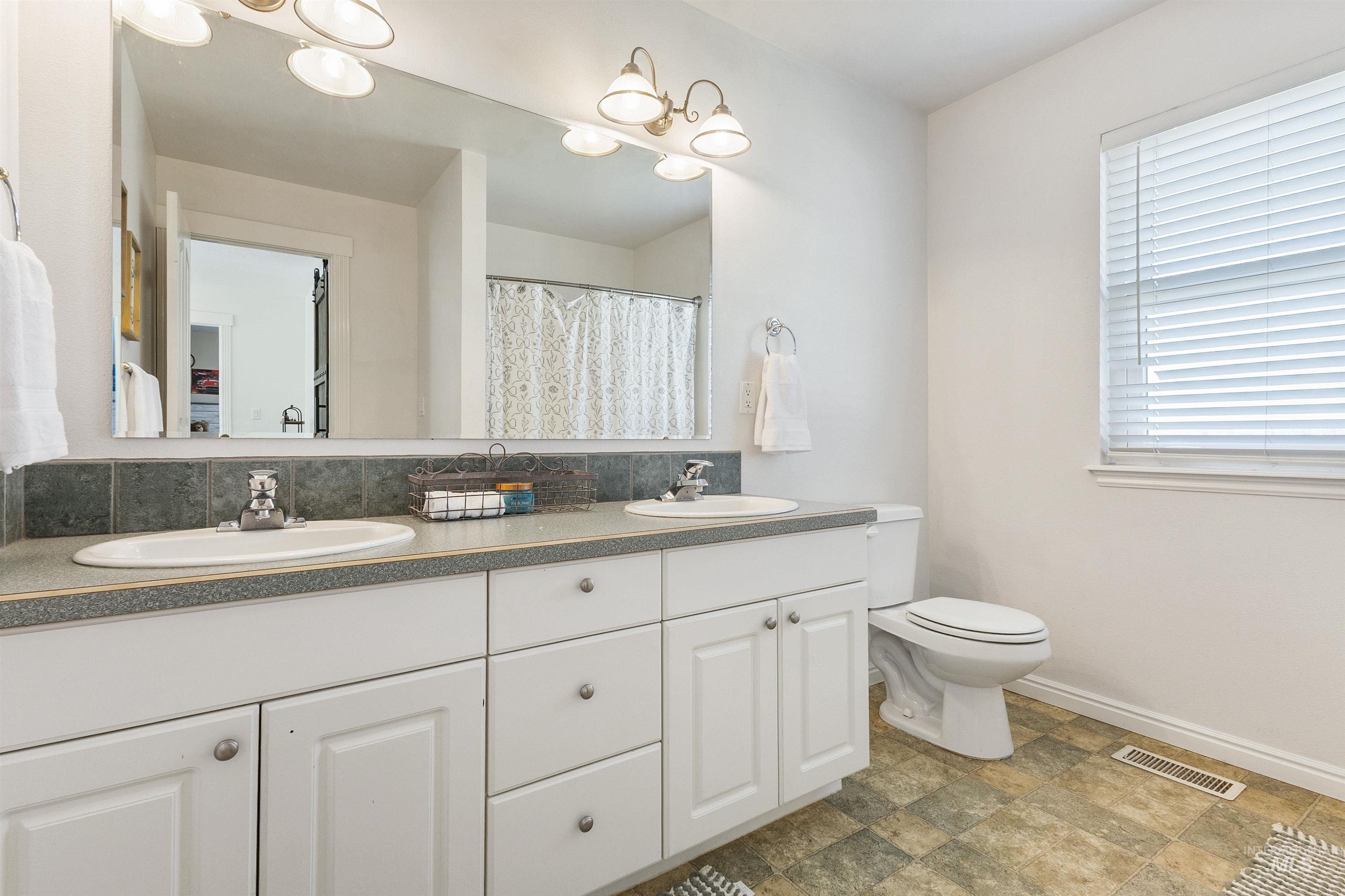 19876 Scotts Lane Caldwell, ID 83607 - Photo 42 of 44 Double vanity with white cabinetry, dual undermount sinks, and a dark stone-look countertop