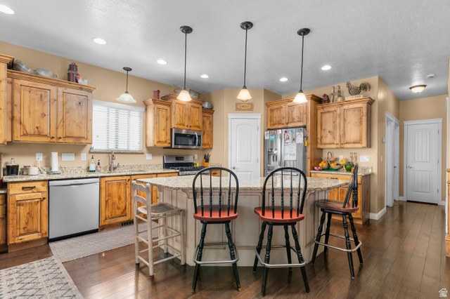 5702 950 North Ogden, UT 84404 - Photo 17 of 36 Kitchen featuring a central island with a built-in breakfast bar, granite countertops, wood-finish cabinetry, stainless steel appliances, and wood-finish flooring