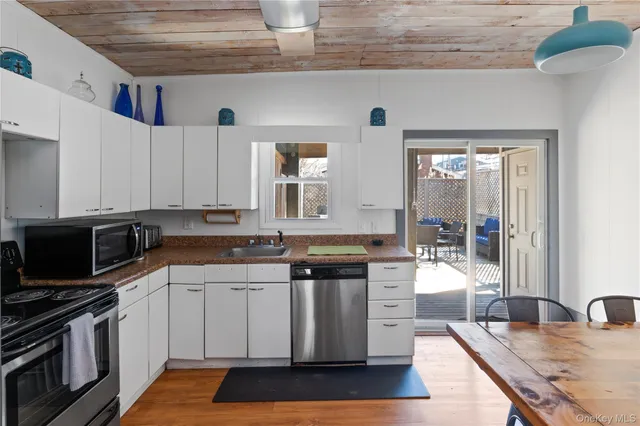 a kitchen with stainless steel appliances granite countertop a stove a sink dishwasher and white cabinets with wooden floor