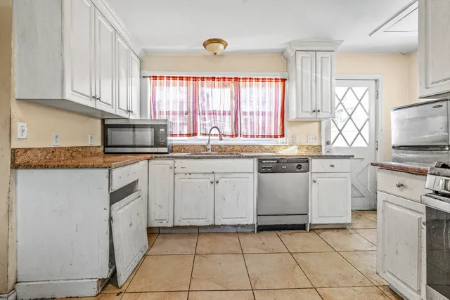 a kitchen with white cabinets appliances a sink and a window